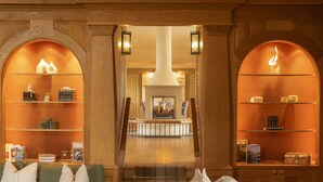 Een hotel lobby met een open haard, houten wandplanken met decoratieve objecten, en een trap naar een hoger gelegen verdieping.