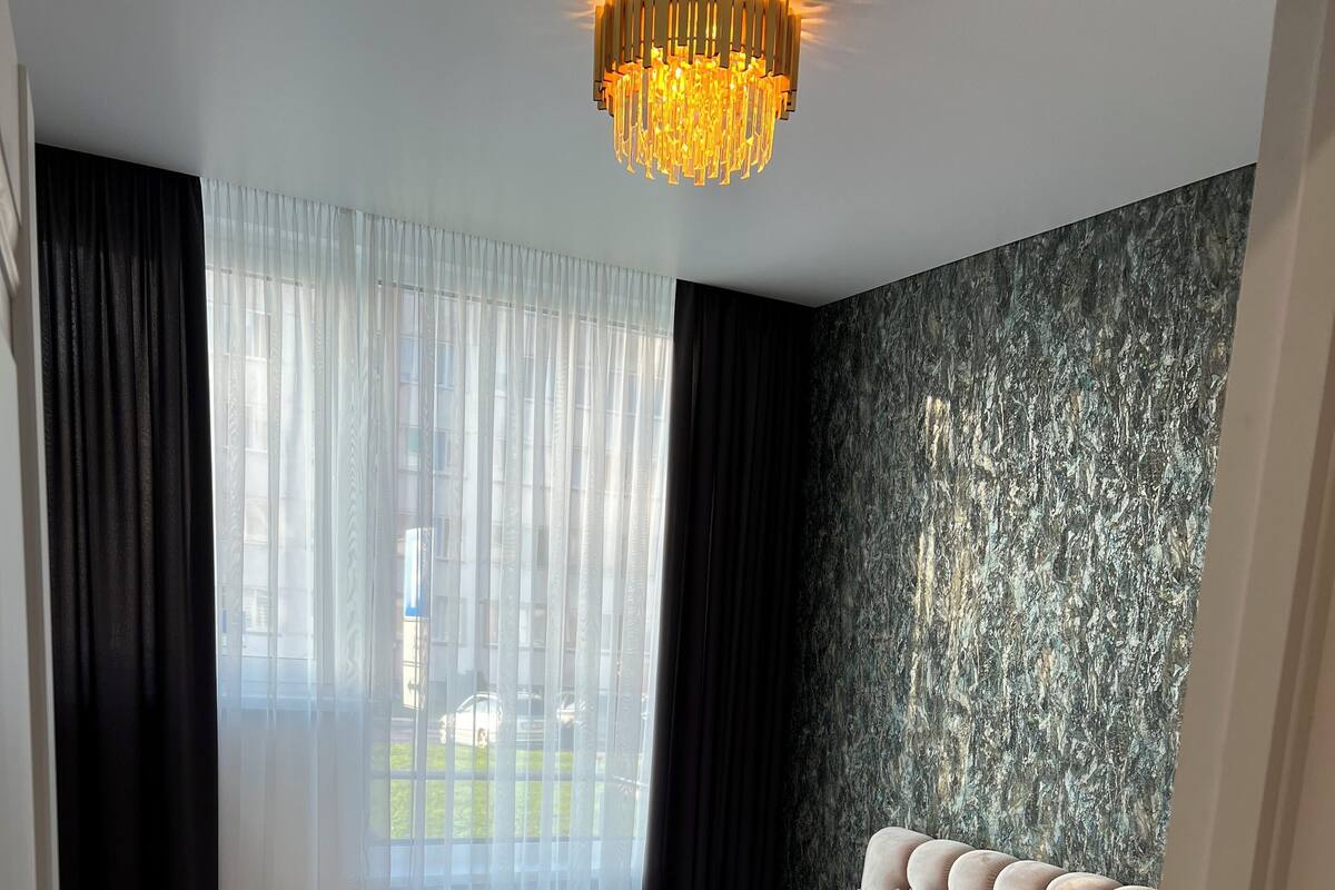 A modern bedroom with a large bed, a chandelier, and a view of the outside.