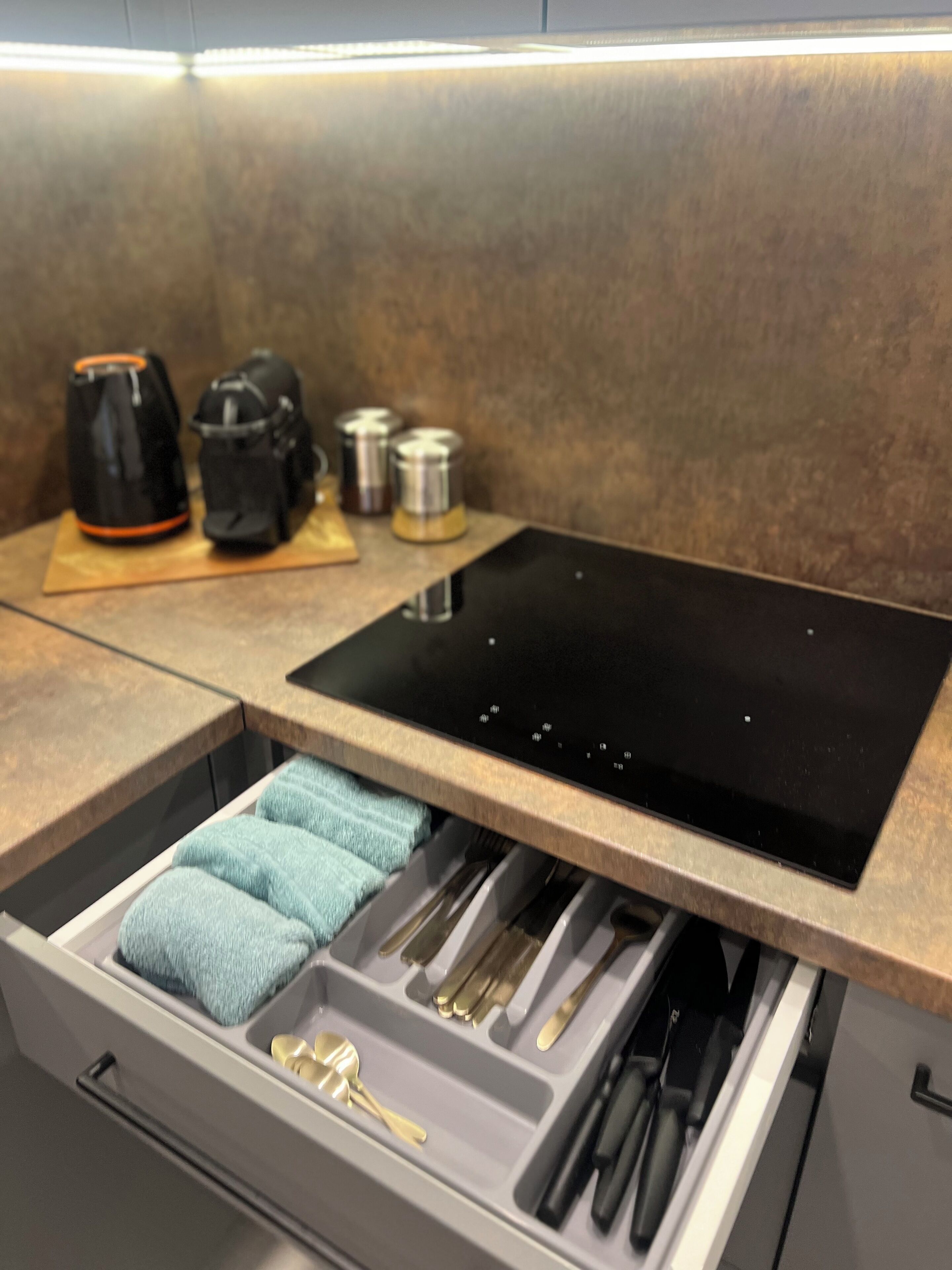 A kitchen with a built-in stove, a drawer with utensils, and a coffee maker on the countertop.