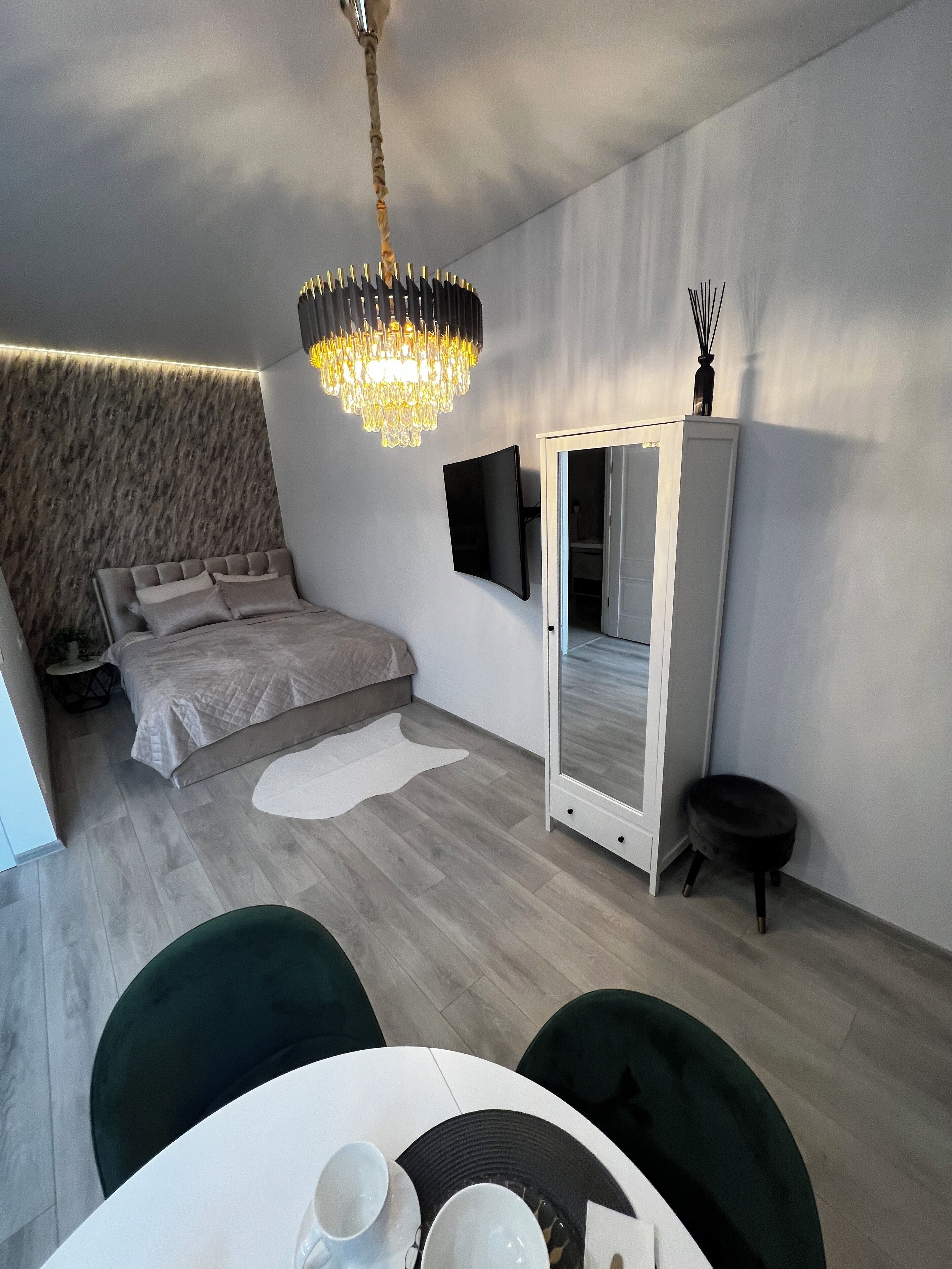 Un dormitorio moderno con una cama, un espejo grande, una araña y un comedor con mesa y sillas.