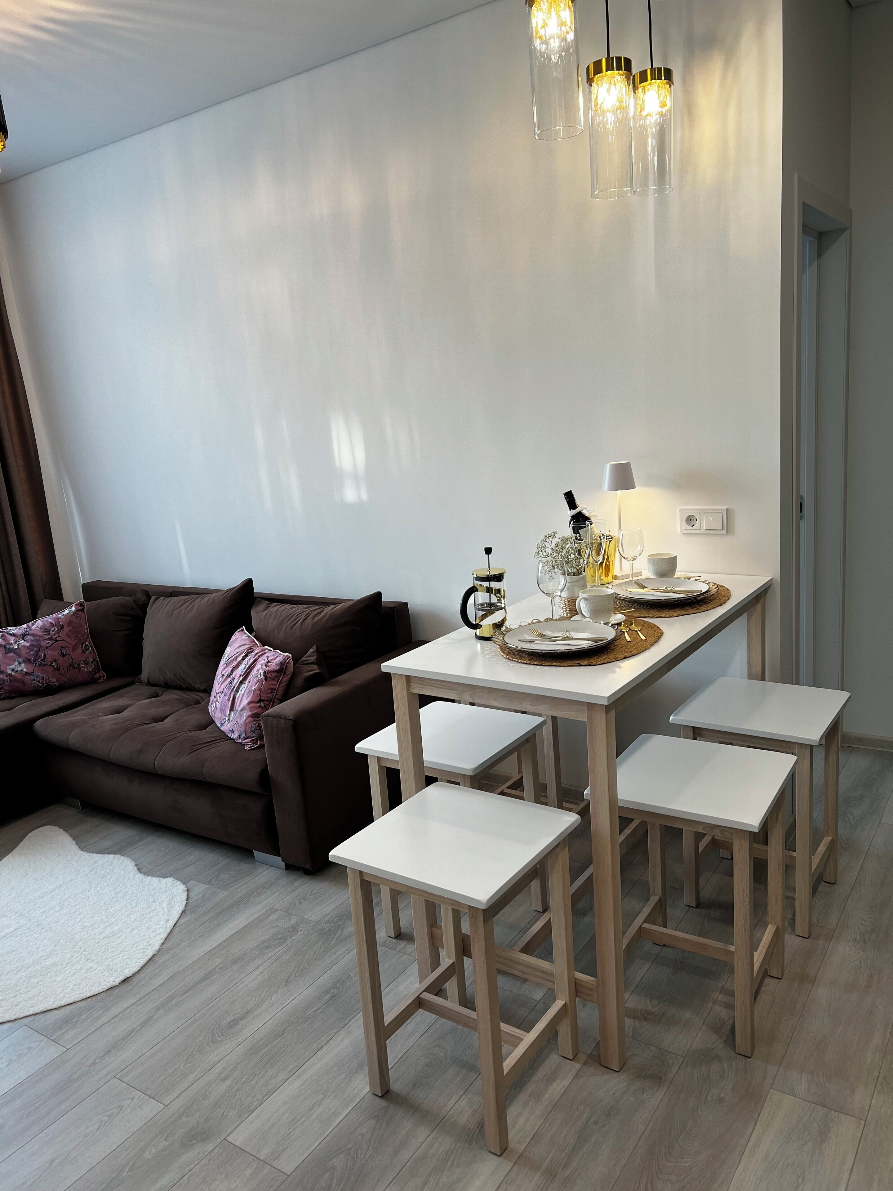 A modern living room with a brown sofa, a dining table with chairs, and a hanging light fixture.