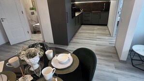 Ein moderner Essbereich mit einem runden Tisch, gedeckt für vier Personen, einer darüber hängenden Chandelierleuchtre und Blick in eine Küche mit dunklen Schränken.