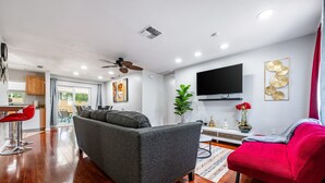 Un salon moderne avec un canapé gris, un fauteuil rouge et un téléviseur à écran plat fixé au mur.