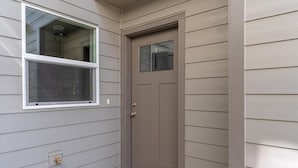 A house with a beige front door, a window with a white frame, and a small porch area. - Flexible Extended Stay 3BR - Spacious + Fireplace + Patio (Salem)