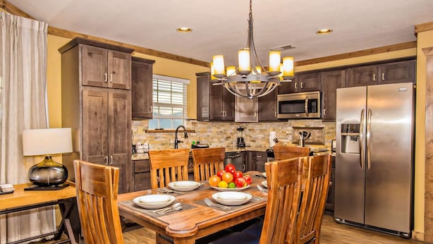 A modern kitchen with wooden cabinets, a stainless steel refrigerator, and a dining table set for four. - Rustic 2BR Condo w/ Views & Full Kitchen (Pigeon Forge)