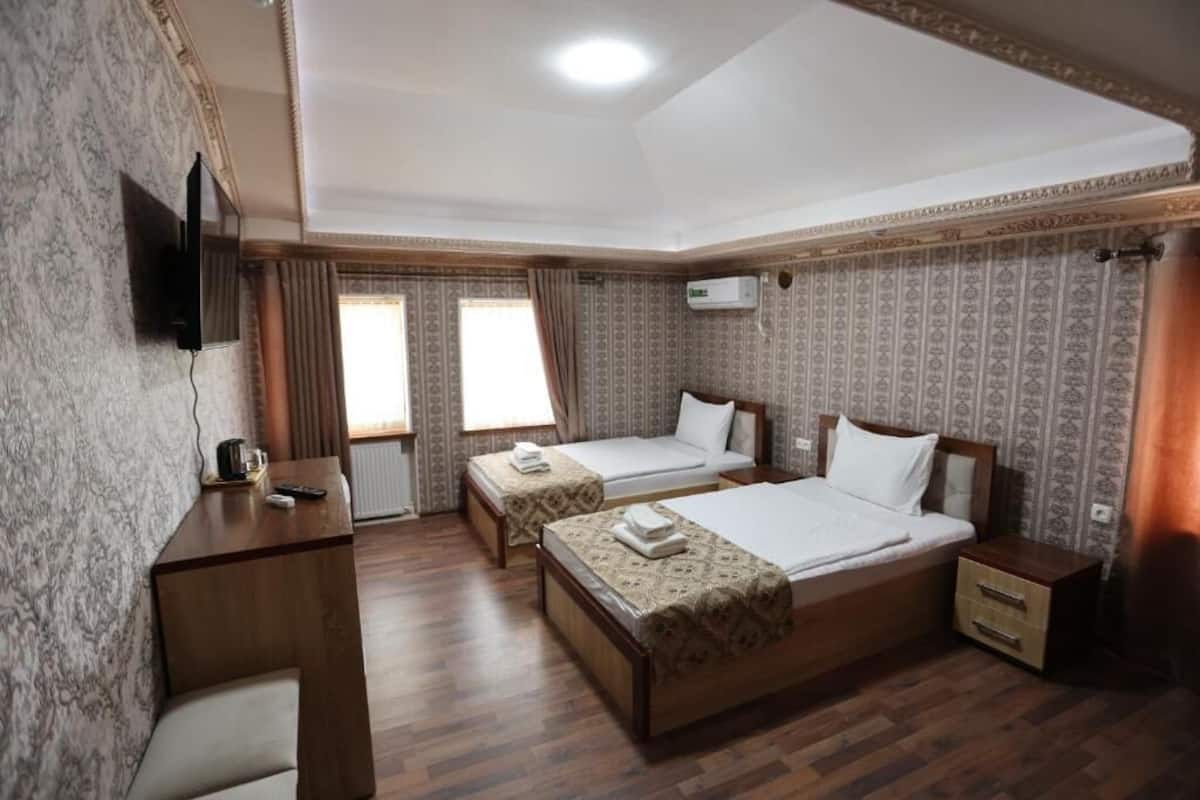 A hotel room with two beds, a desk, a TV, and an air conditioning unit.