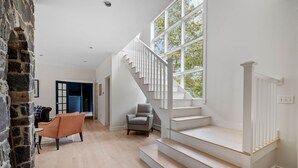 Ein geräumiger Wohnbereich mit einer Treppe zu einer oberen Etage, einer Steinwand und einem großen Fenster, das für natürliches Licht sorgt.