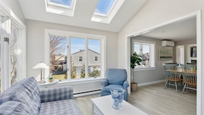 A modern living room with a sofa, a coffee table, and a chair. There are skylights, a window, and a view of the outside. - Surfside Sanctuary at Gooch's Beach (Kennebunk)