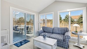 A modern living room with a checkered sofa, a white coffee table, and a glass door leading to an outdoor deck. - Surfside Sanctuary at Gooch's Beach (Kennebunk)