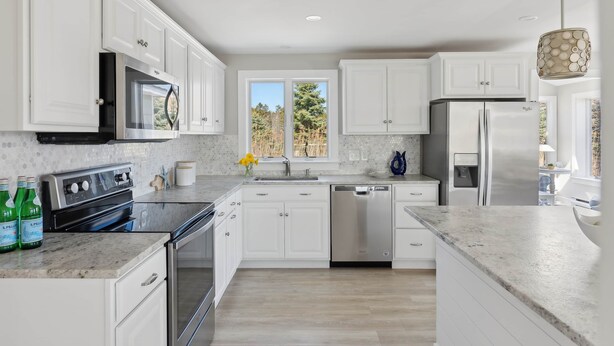 A modern kitchen with white cabinets, stainless steel appliances, and a large window. - Surfside Sanctuary at Gooch's Beach (Kennebunk)