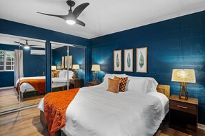 Une chambre d’hôtel avec un grand lit, deux tables de chevet, un ventilateur de plafond et une fenêtre avec des rideaux.