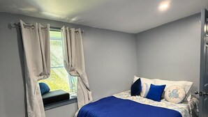 Ein Schlafzimmer mit einem Bett, einem Fenster mit Vorhängen, einer Tür und einem Fliesenboden.