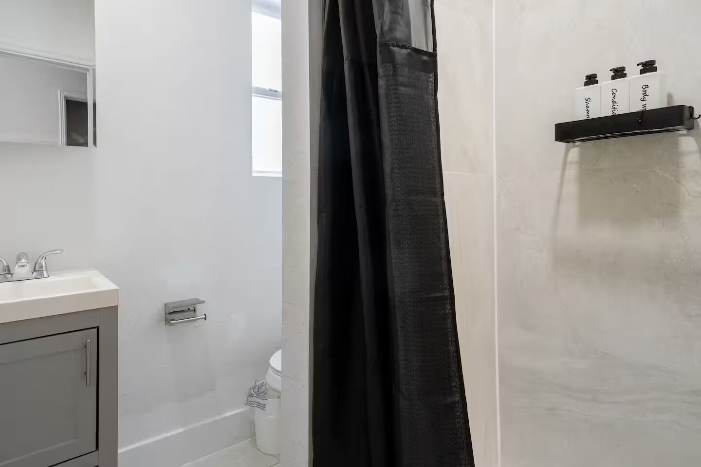 Une salle de bain avec un lavabo blanc, un miroir, un rideau de douche et une étagère contenant des articles de toilette.