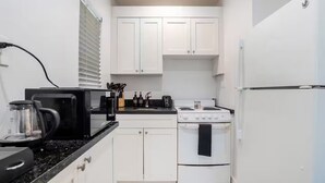 A compact kitchen with white cabinets, a black countertop, a stove, and a refrigerator. - Stylish Stay Minutes from Wynwood & Midtown (Miami)