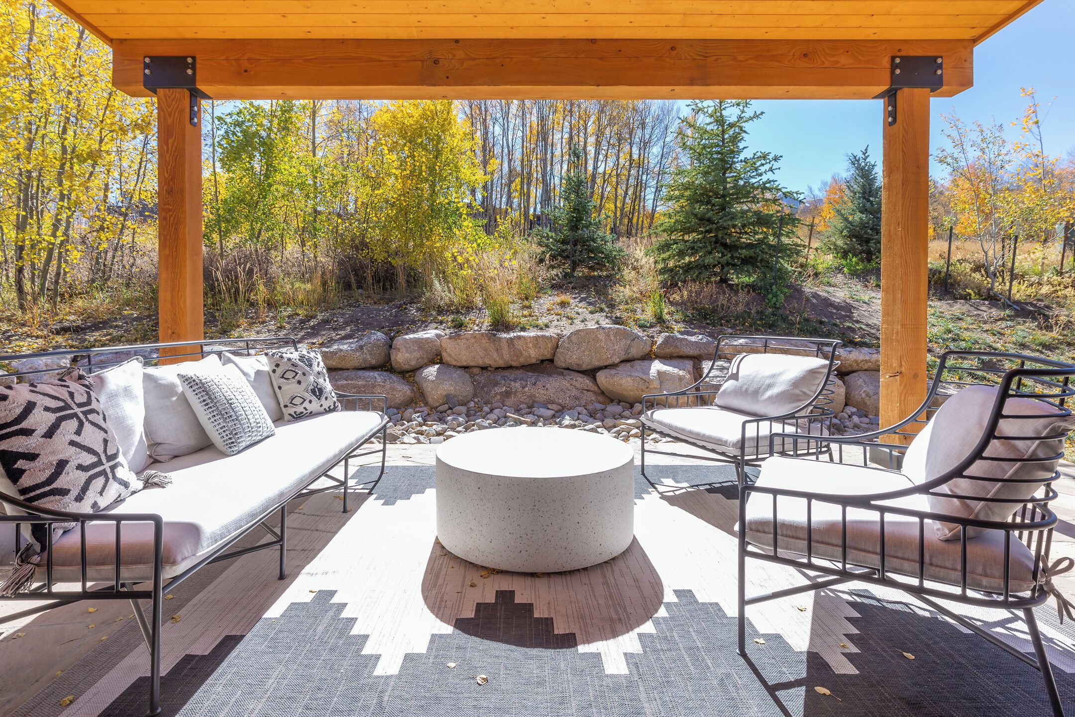 An outdoor seating area with a round table, cushioned chairs, and a wooden pergola.