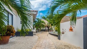 A pathway leading to a building with a thatched roof, surrounded by palm trees and potted plants. - Welcome To Casa Sabean, a Paradise in Paramira! 4 Bedroom with Pool (Oranjestad)