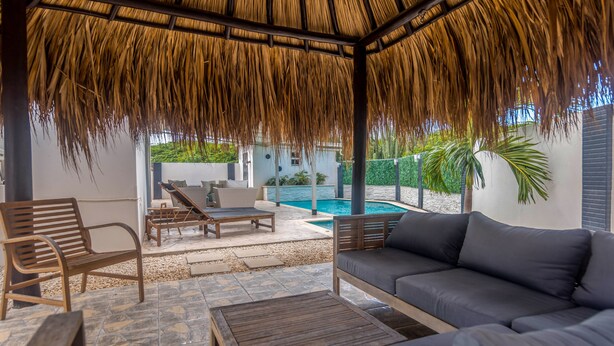 A covered outdoor seating area with a pool in the background. - Welcome To Casa Sabean, a Paradise in Paramira! 4 Bedroom with Pool (Oranjestad)
