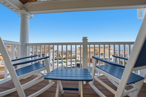 Een balkon met witte leuningen en blauwe stoelen, met uitzicht op een woonwijk met huizen en een zwembad.