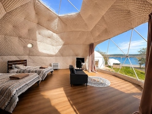 A spacious room with a high ceiling, a bed, a desk, and a view of the sea. - Baddeck Domes (Baddeck)