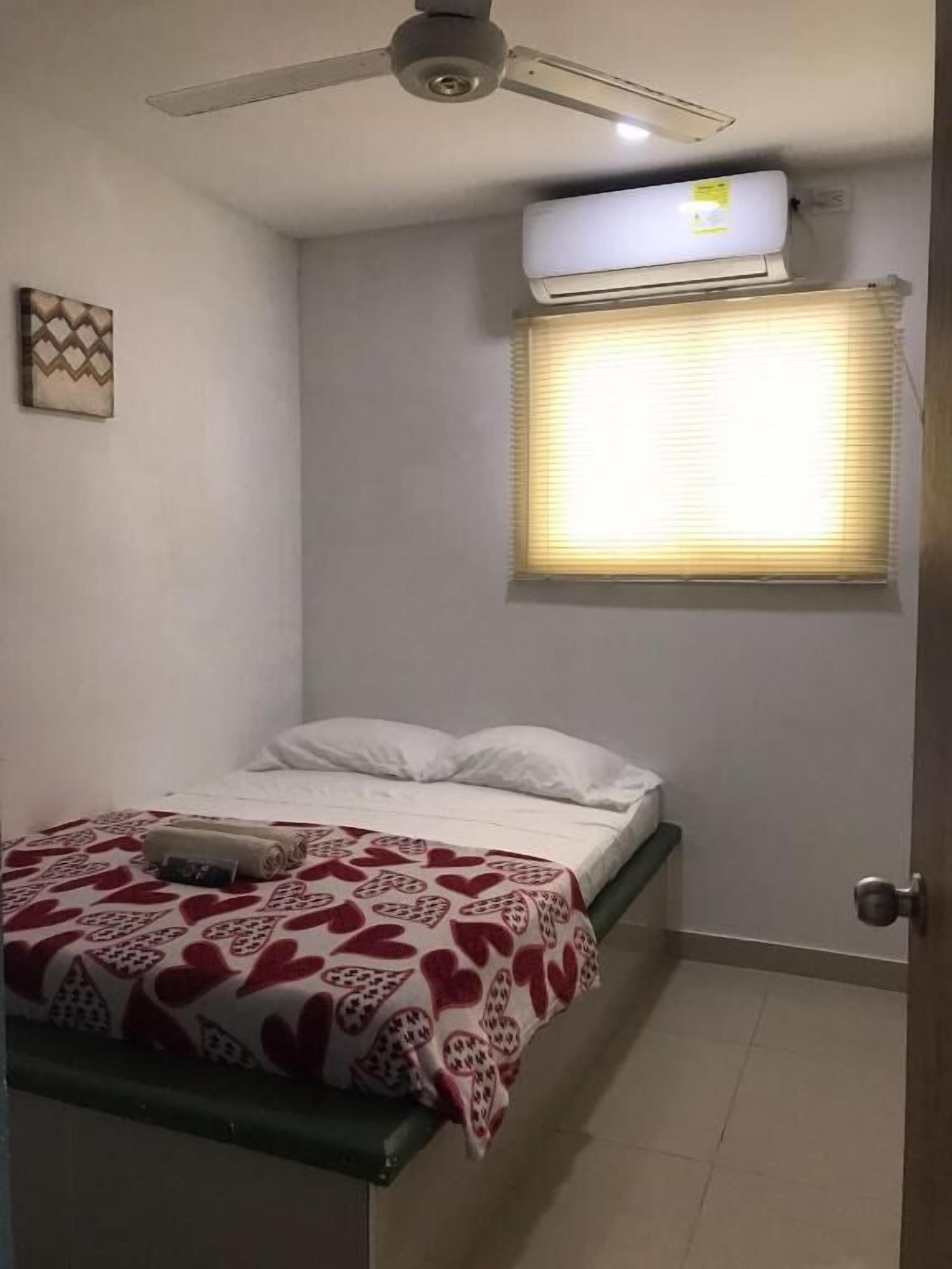 Un dormitorio con cama, ventilador de techo, aire acondicionado, ventana con persianas y puerta.