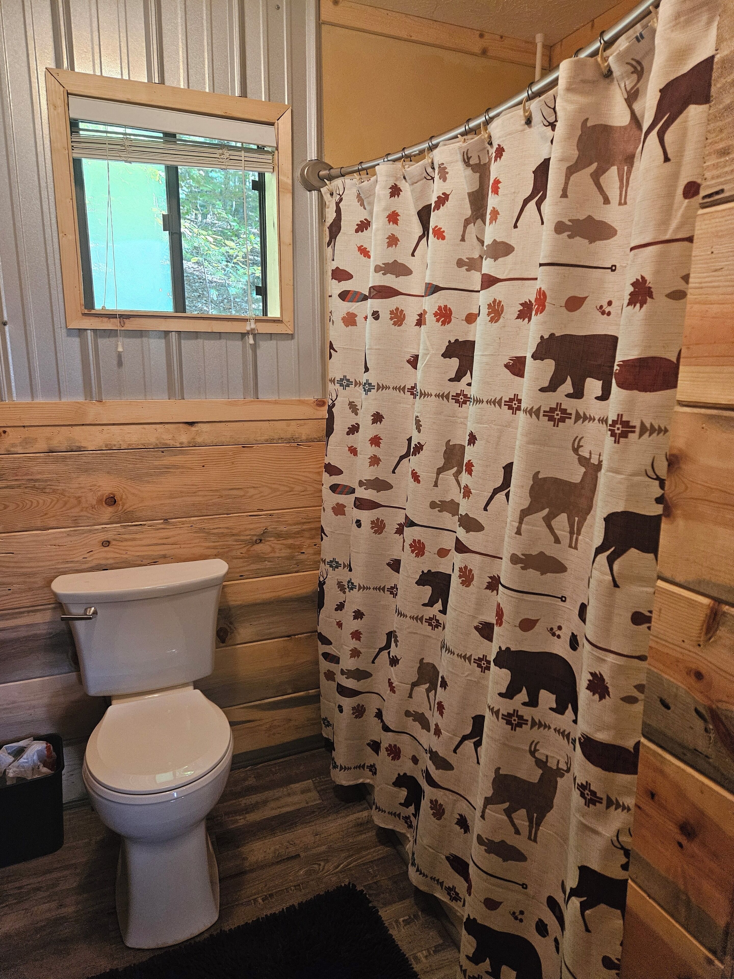 A bathroom with a toilet, wooden walls, a window, and a shower curtain with animal prints.