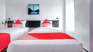 Een hotelkamer met twee bedden, elk met rode en witte beddengoed, en een schilderij aan de muur.
