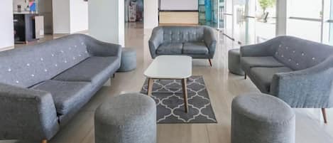 A modern hotel lobby with grey sofas, ottomans, and a white coffee table.