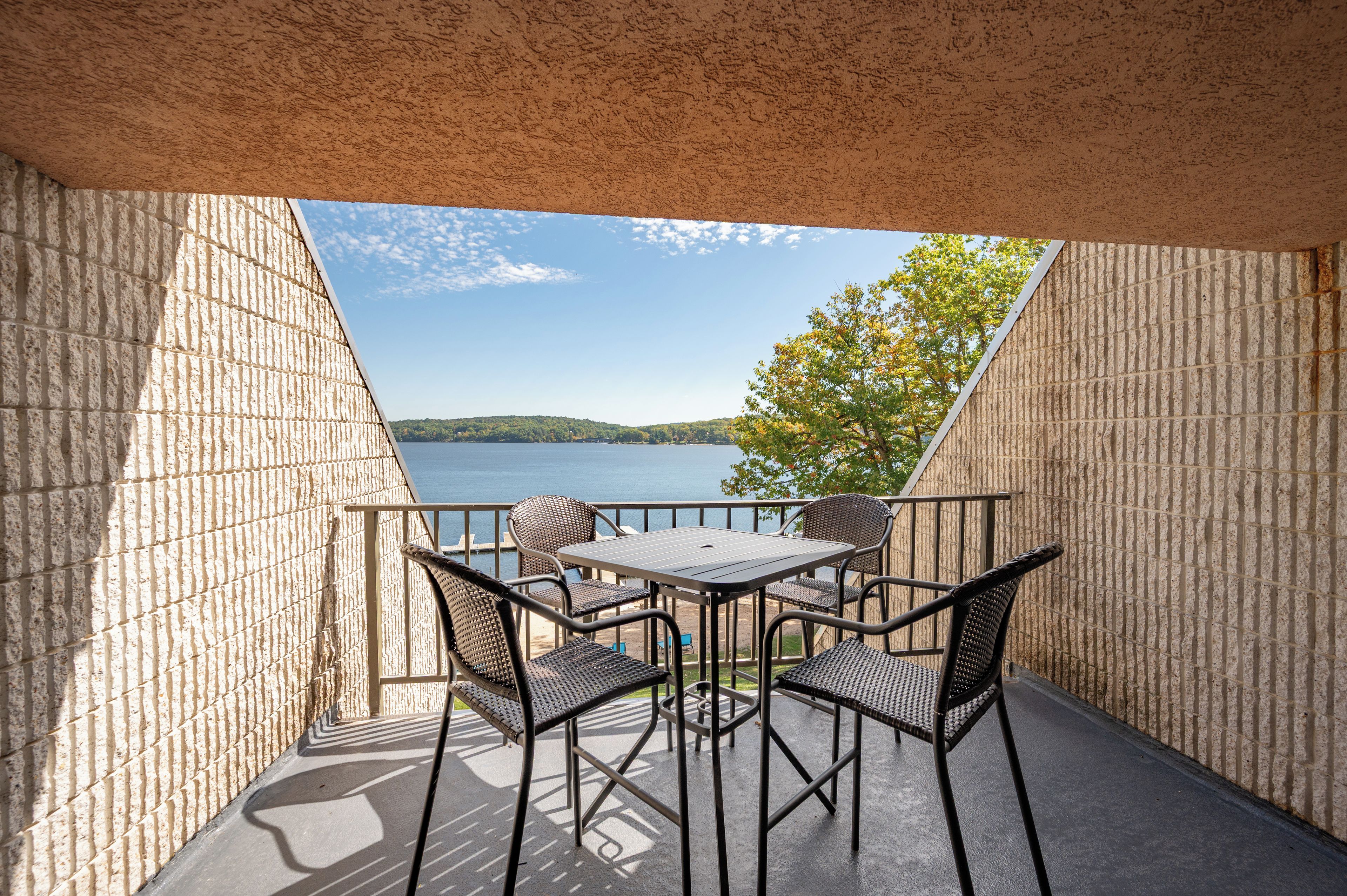 A balcony with a table and chairs, overlooking a body of water and a distant hill.