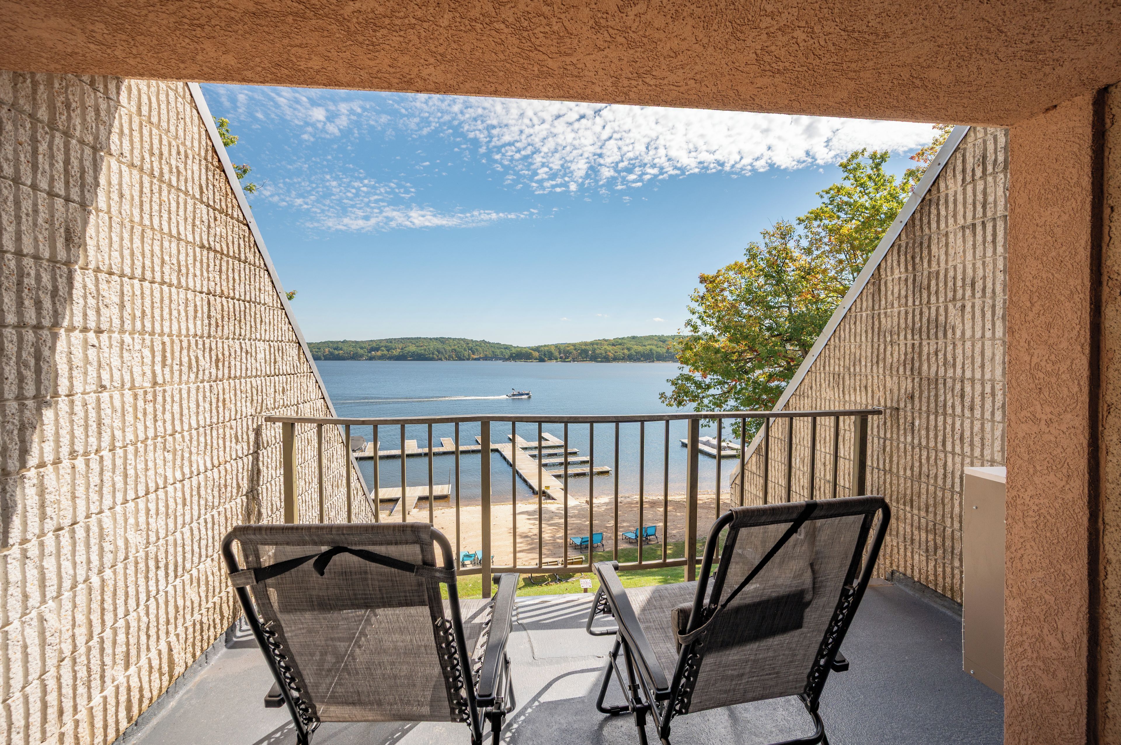 A balcony with two chairs, a view of a lake, and a dock with boats.