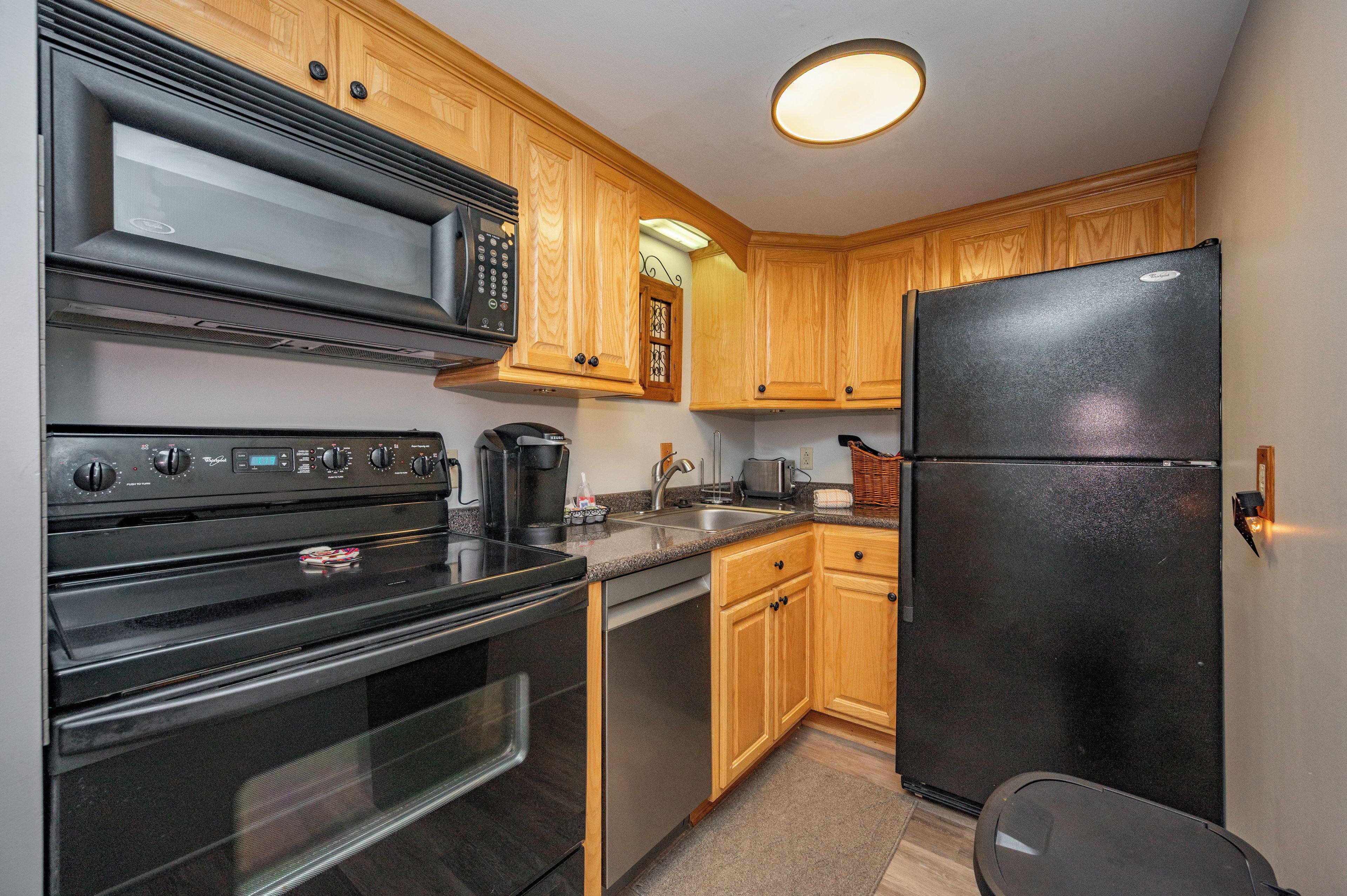 A kitchen with wooden cabinets, a black refrigerator, a microwave, an oven, and a coffee maker.