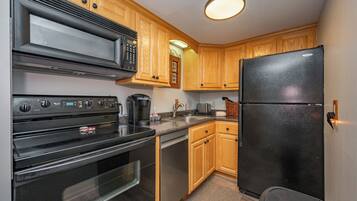 A kitchen with wooden cabinets, a black refrigerator, a microwave, an oven, and a coffee maker.