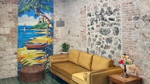A room with a high ceiling, exposed brick walls, a yellow sofa, a green tiled floor, a mosaic painting, and a skylight. - Treehouse - The Canopy (Christiansted)