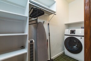 A laundry area with a washing machine, ironing board, and hanging rack.