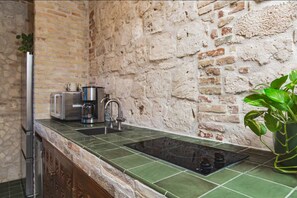 A kitchen with a brick wall, a green countertop, a sink, a stove, and a potted plant.