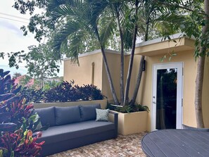 A modern outdoor seating area with a grey sofa, a small table, and a planter with various plants. - Treehouse - The Canopy (Christiansted)
