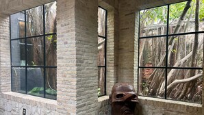 A room with stone walls, large windows, and a wooden sculpture. - Treehouse - The Canopy (Christiansted)