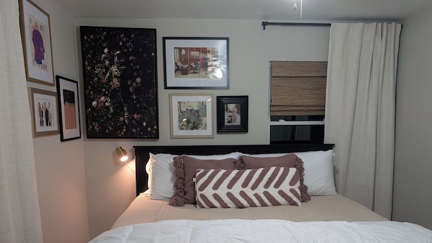 Un lit bien fait, avec une couette blanche et des oreillers, une tête de lit dotée d’un luminaire et des œuvres d’art encadrées accrochées aux murs.
