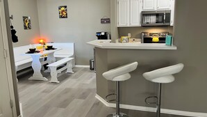 A modern kitchen with white cabinets, a microwave, and a coffee machine. There is a dining area with white benches and a table. - Dog-Friendly Cozy Condo in North Scottsdale! (Scottsdale)