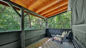 Une véranda couverte avec une chaise suspendue, des balustrades en bois et un tapis à motifs.
