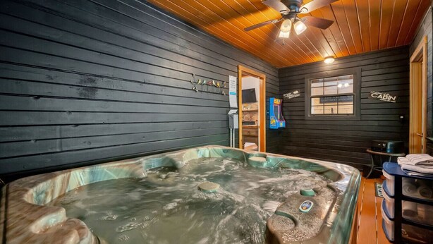 Un bain à remous dans une pièce aménagée comme une cabane, avec des murs en bois et un ventilateur de plafond.