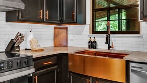 Une cuisine moderne avec des meubles de couleur sombre, une cuisinière en acier inoxydable, un évier en cuivre et une fenêtre donnant sur un paysage verdoyant.