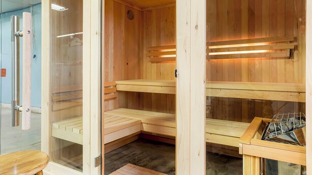 Een houten sauna met glazen deuren, meerdere banken en verlichting in het plafond.