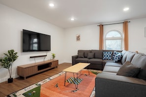 A modern living room with a flat-screen TV, a sofa, a coffee table, and a patterned rug.