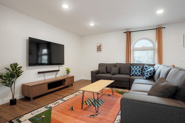 Una sala de estar moderna con un televisor de pantalla plana, un sofá, una mesa de centro y una alfombra estampada.