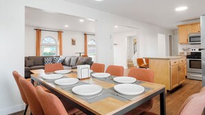 Een moderne keuken met inbouwapparatuur, een eethoek met een tafel voor vier personen, en een zithoek met een bank en gordijnen.