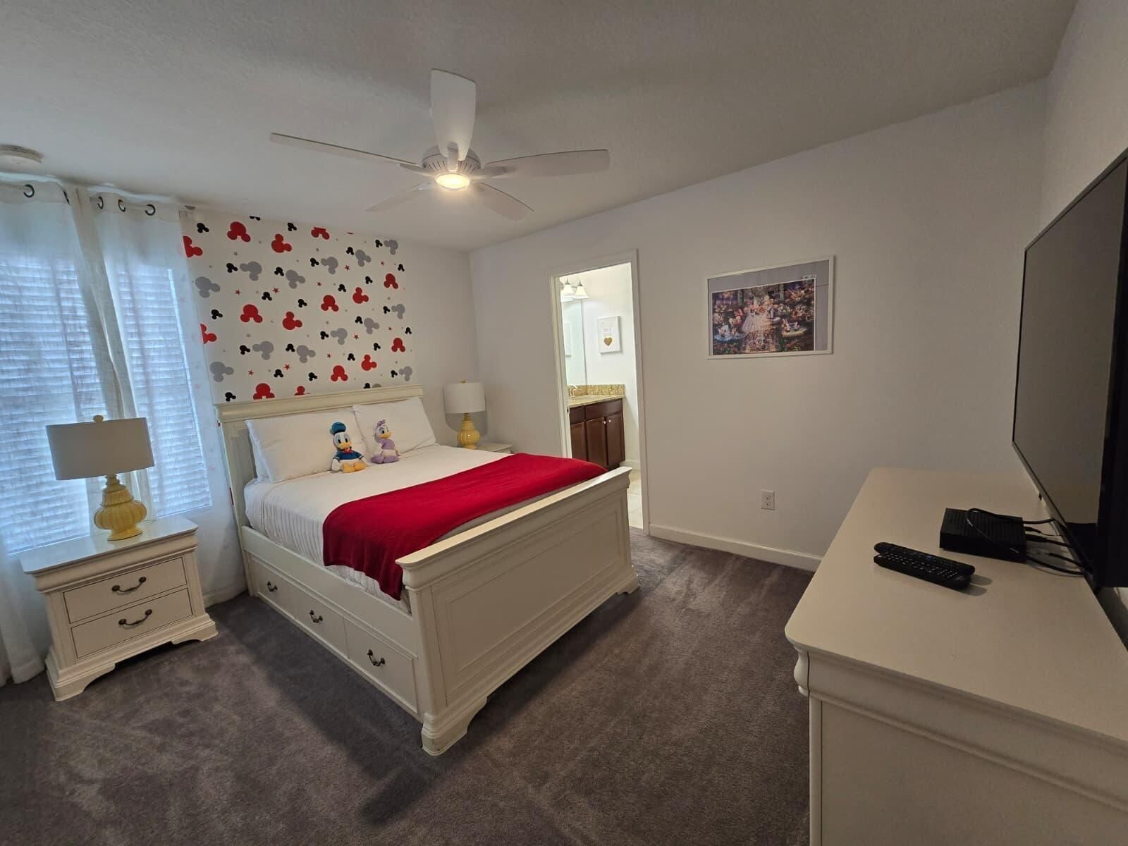 A bedroom with a bed, bedside tables, a ceiling fan, a TV, and a wall with a picture.