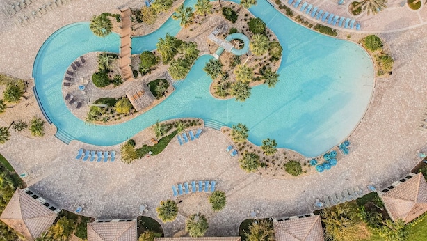 An aerial view of a resort with a large, winding pool surrounded by palm trees and sun loungers. - 6-bedroom Private Pool House Championsgate (Davenport)