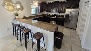 A modern kitchen with dark cabinets, stainless steel appliances, and a granite island with bar stools. - 6-bedroom Private Pool House Championsgate (Davenport)