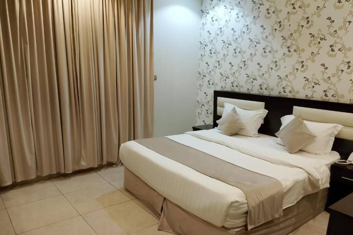 Une chambre d’hôtel avec un lit, des rideaux, une table de chevet et un mur recouvert d’un papier peint à motifs floraux.
