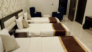 A hotel room with two beds, each with a white bedspread and a brown accent. There are two blue chairs and a small white table. - Diyra Hira (Jeddah)